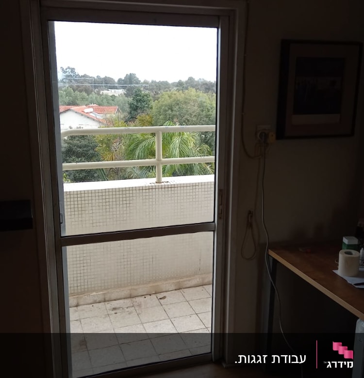 דלת זכוכית פתוחה למרפסת עם נוף ירוק